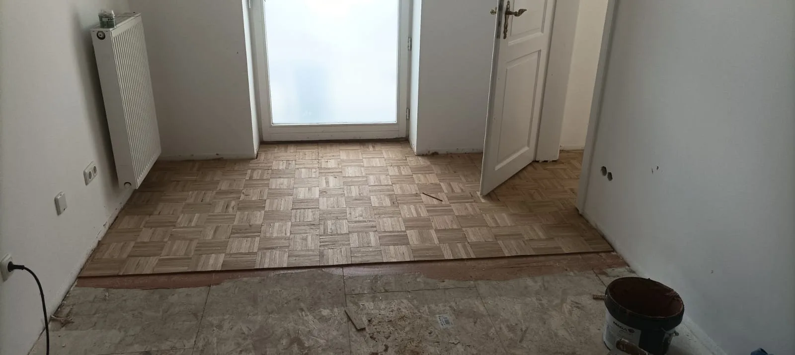 Sicht auf verlegten Parkettboden in einem renovierten Raum mit offener Tür
