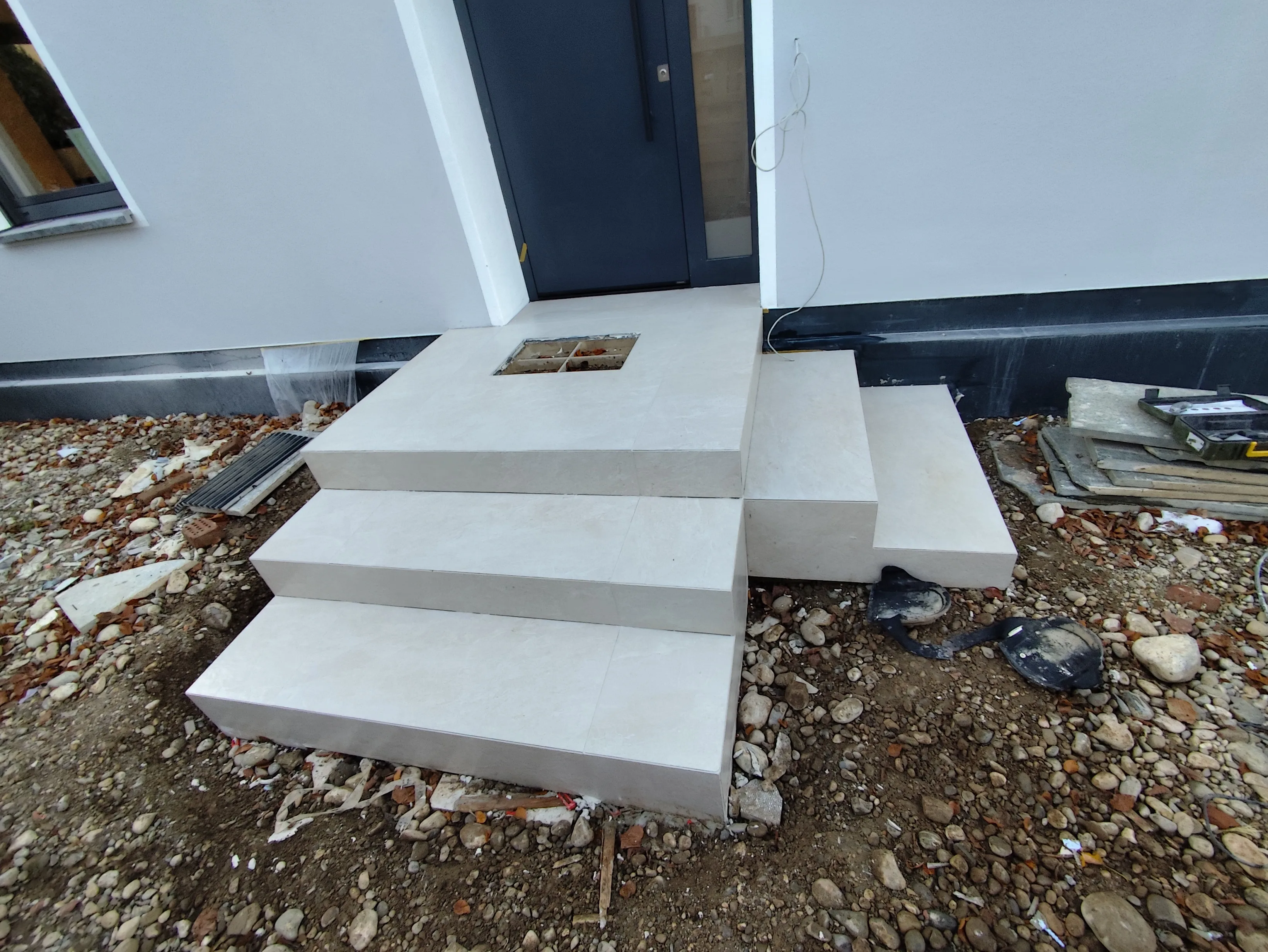 Treppe aus Fliesen mit einer Öffnung für Installation, umgeben von Bauabfällen