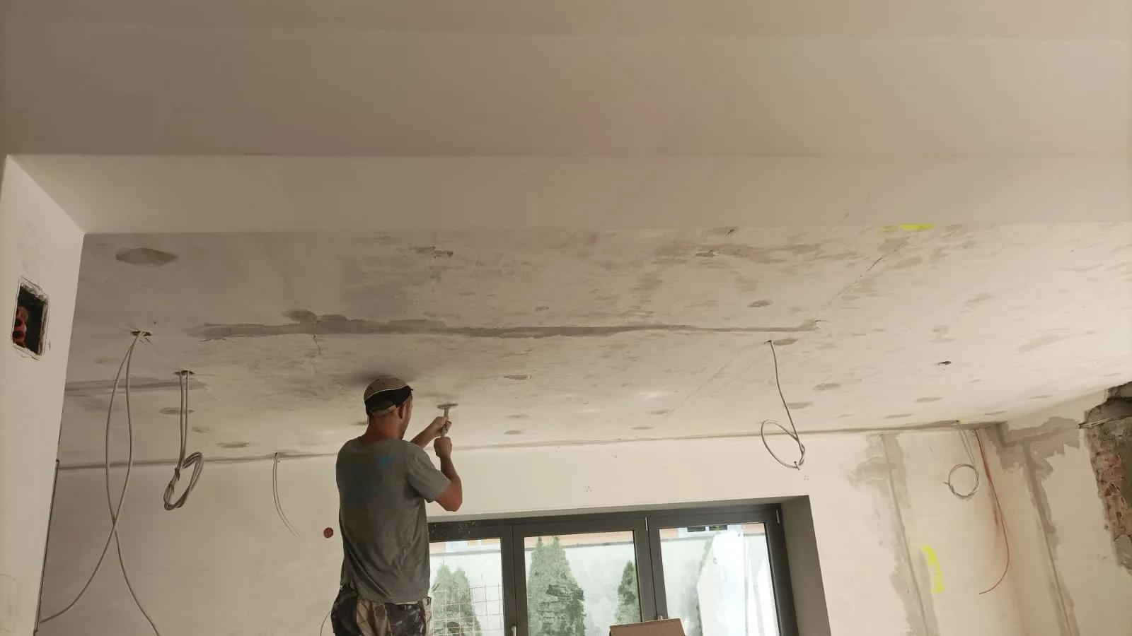 Trockenbauarbeiten an der Decke in einem Wohnraum mit Kabeln und einem Handwerker