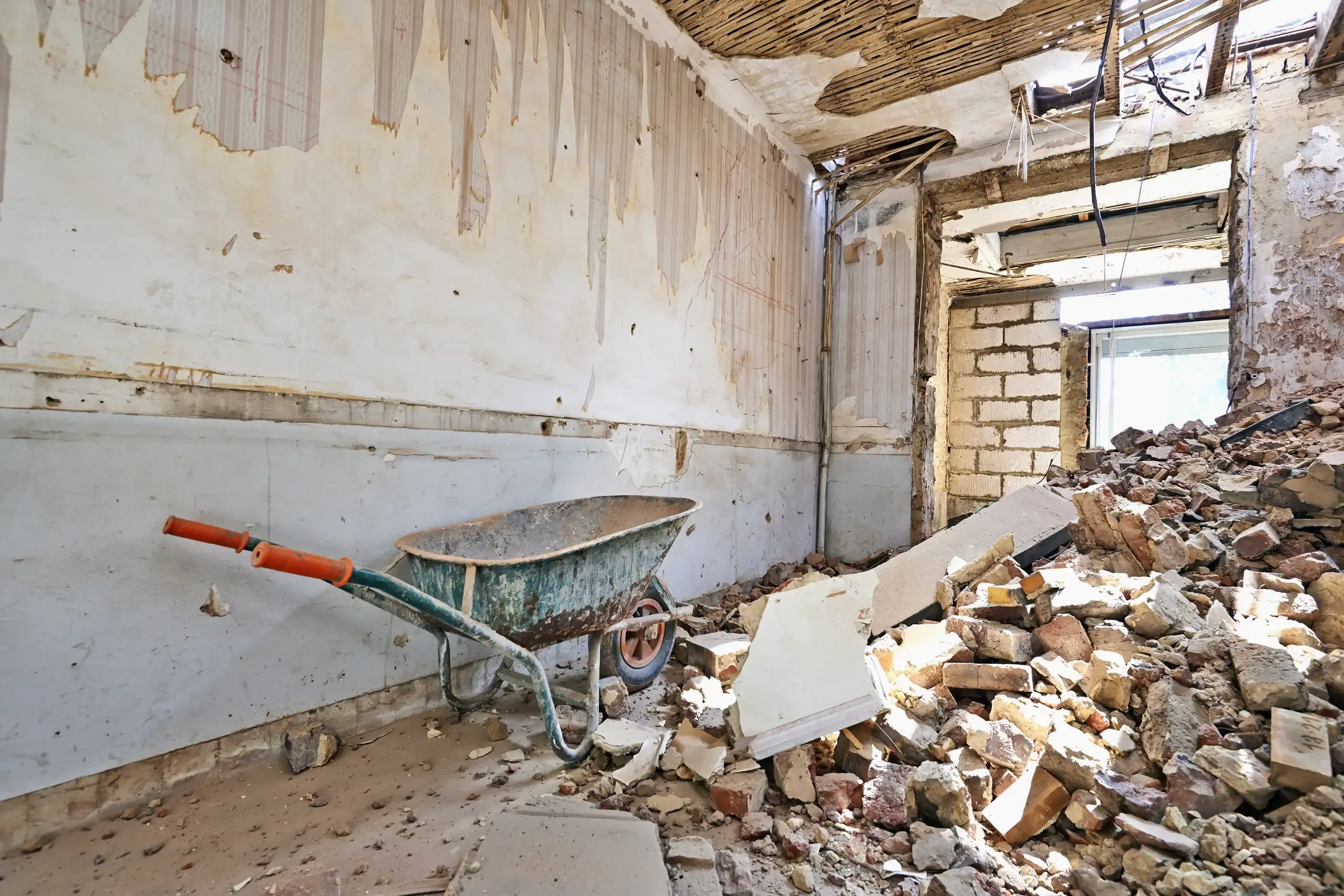 Baustelle mit Abrissarbeiten und Schutt in einem Raum mit Schubkarre