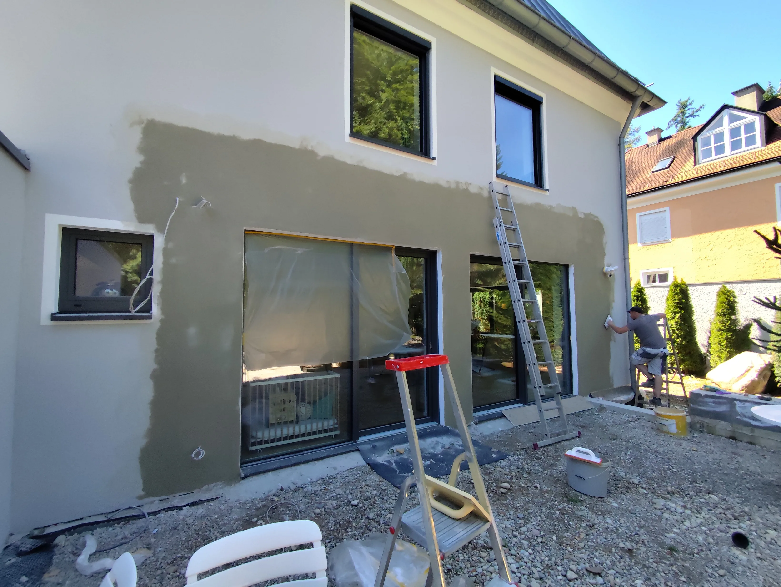 Fassade wird saniert, Arbeiter nutzt eine Leiter, um Putz aufzutragen