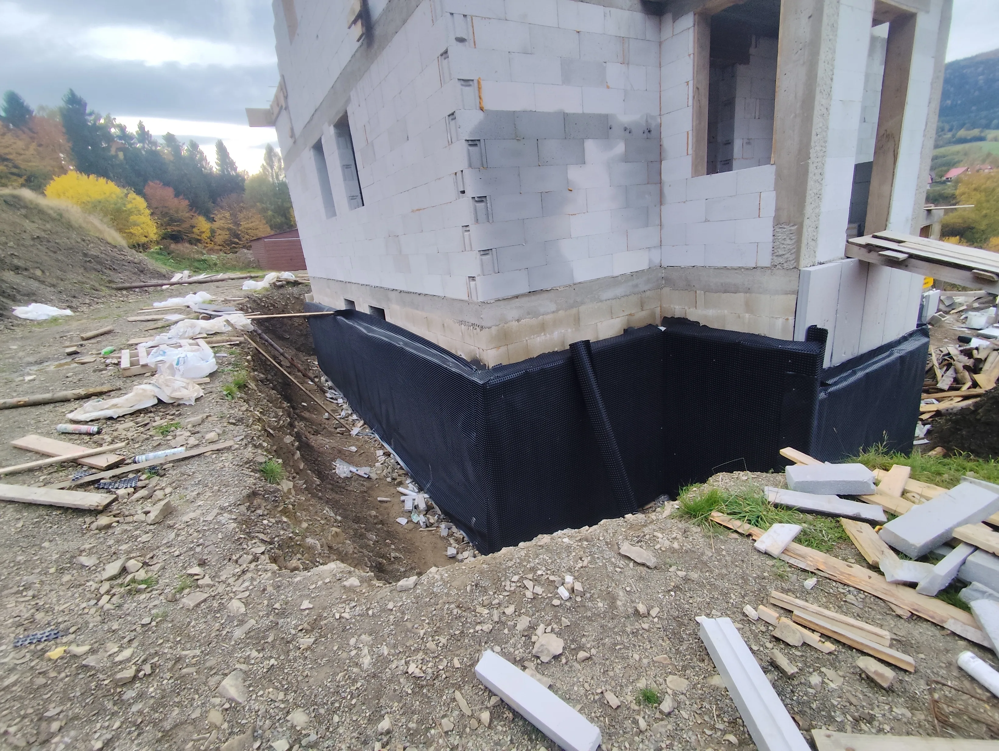 Ansicht eines Baustellenbereichs mit einer unvollendeten Wand und Drainagematerialien