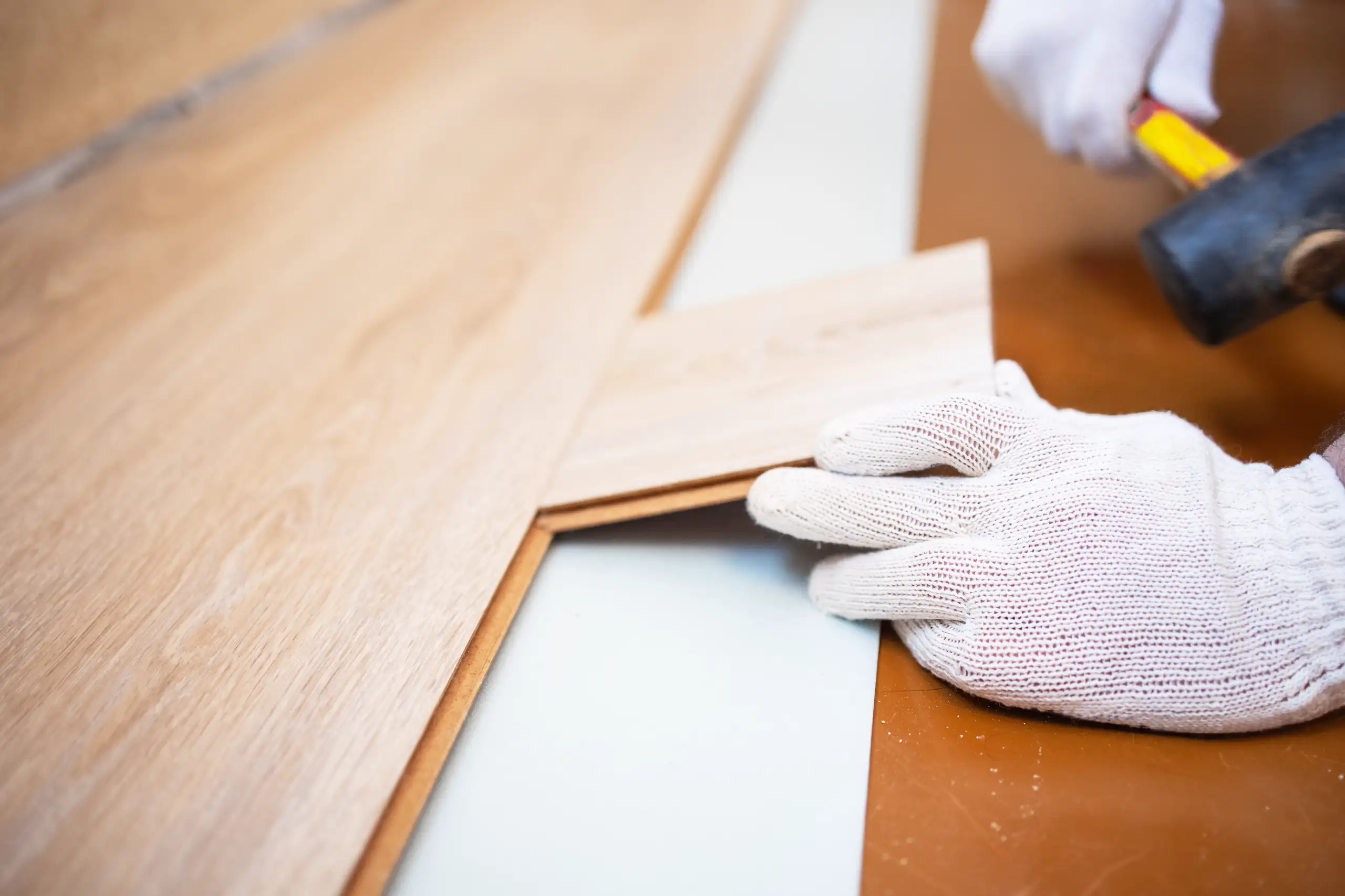 Ein Handwerker verlegt Laminatboden mit einem Hammer auf einer Unterlage